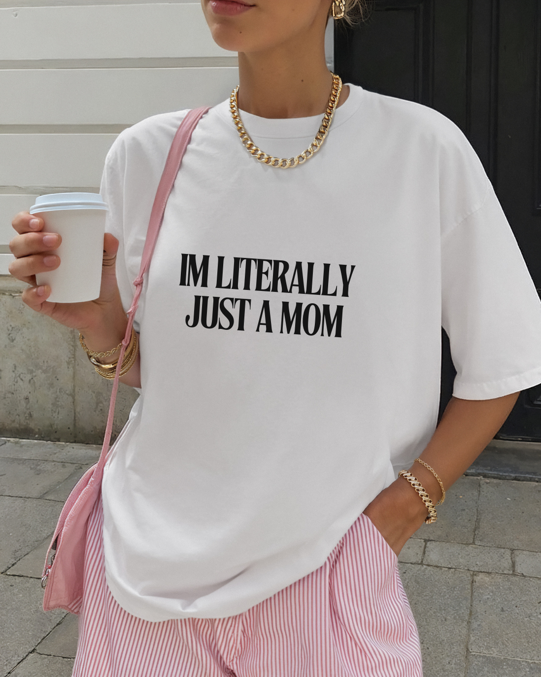 Person wearing a white t-shirt with text 'i'm literally just a mom' and pink shorts, holding a cup.