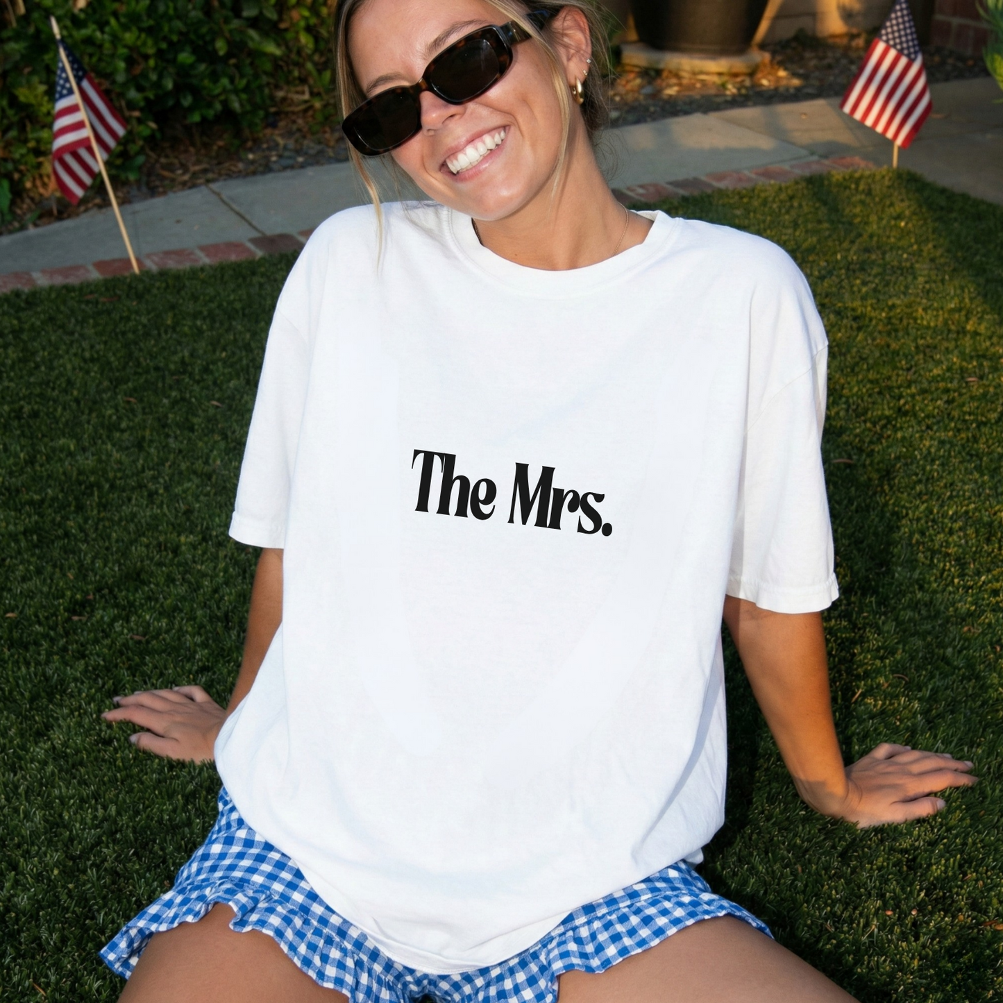 Woman wearing a white t-shirt with 'The Mrs.' text, sitting on grass.