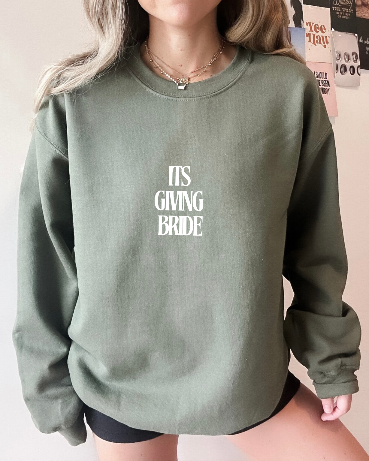 Person wearing a green sweatshirt with 'IT'S GIVING BRIDE' text.
